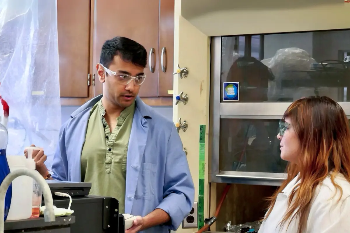 Two researchers wearing safety glasses and lab coats work together at a laboratory bench.