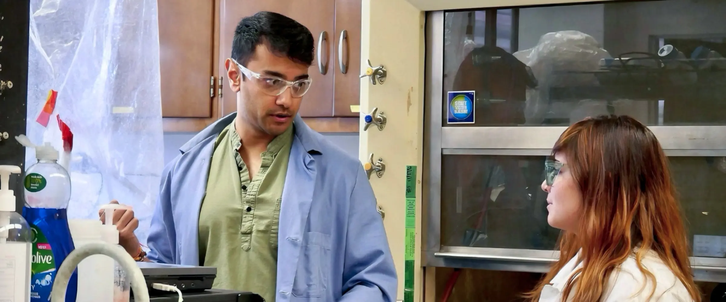 Two researchers wearing safety glasses and lab coats work together at a laboratory bench.