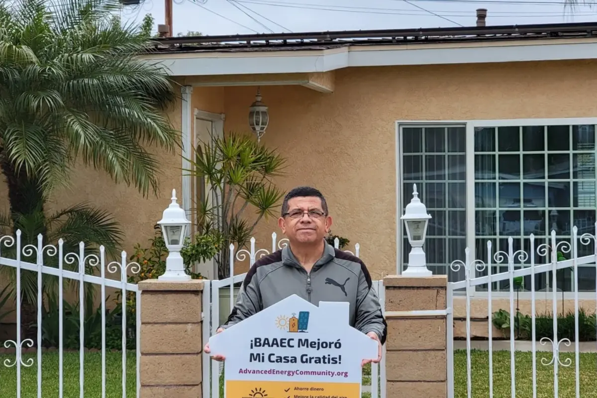 BAAEC participant stands in front of gated home with a yard sign explaining the advanced energy community program.