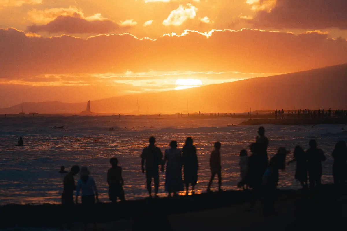 People silhouetted against an orange sunset over the ocean.