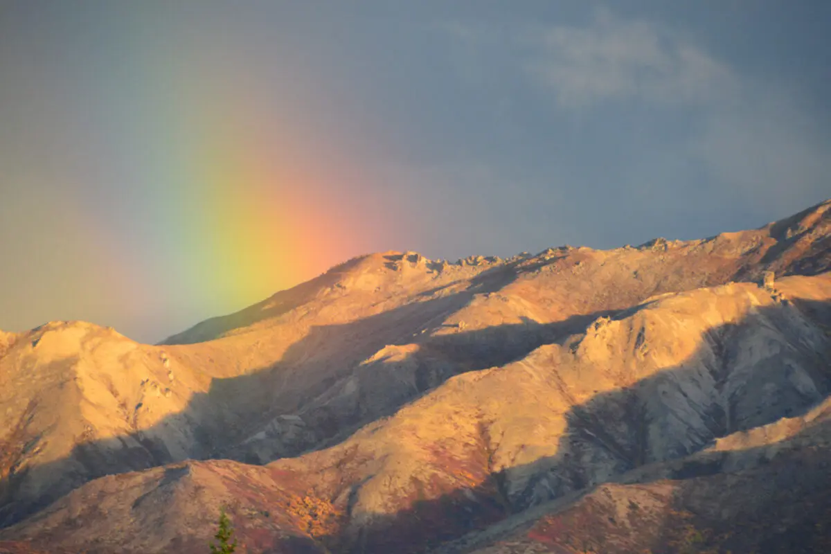 Sunlit desert mountains beneath a rainbow.